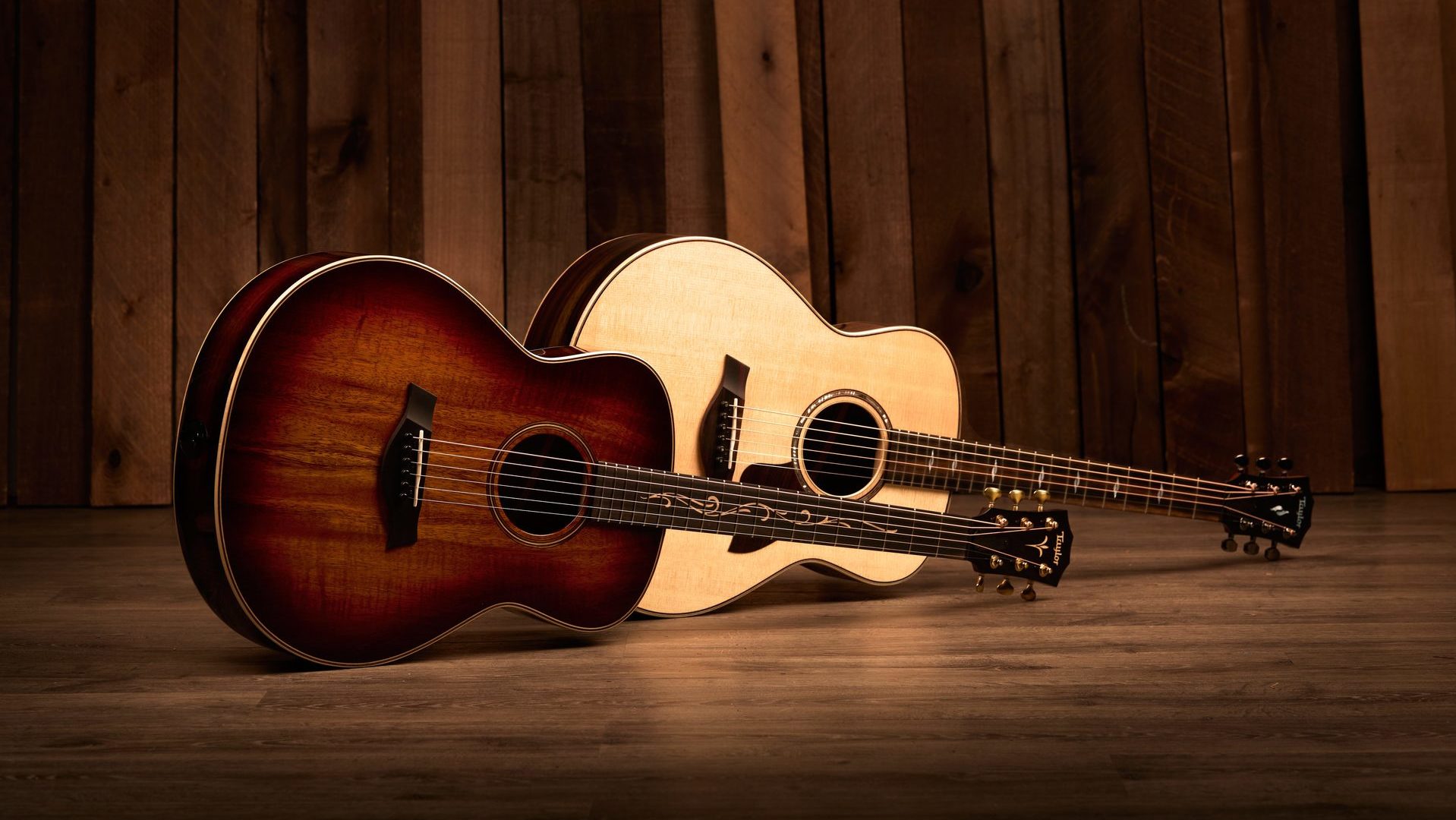 two Taylor GT acoustic guitars photographed horizontally with wood background