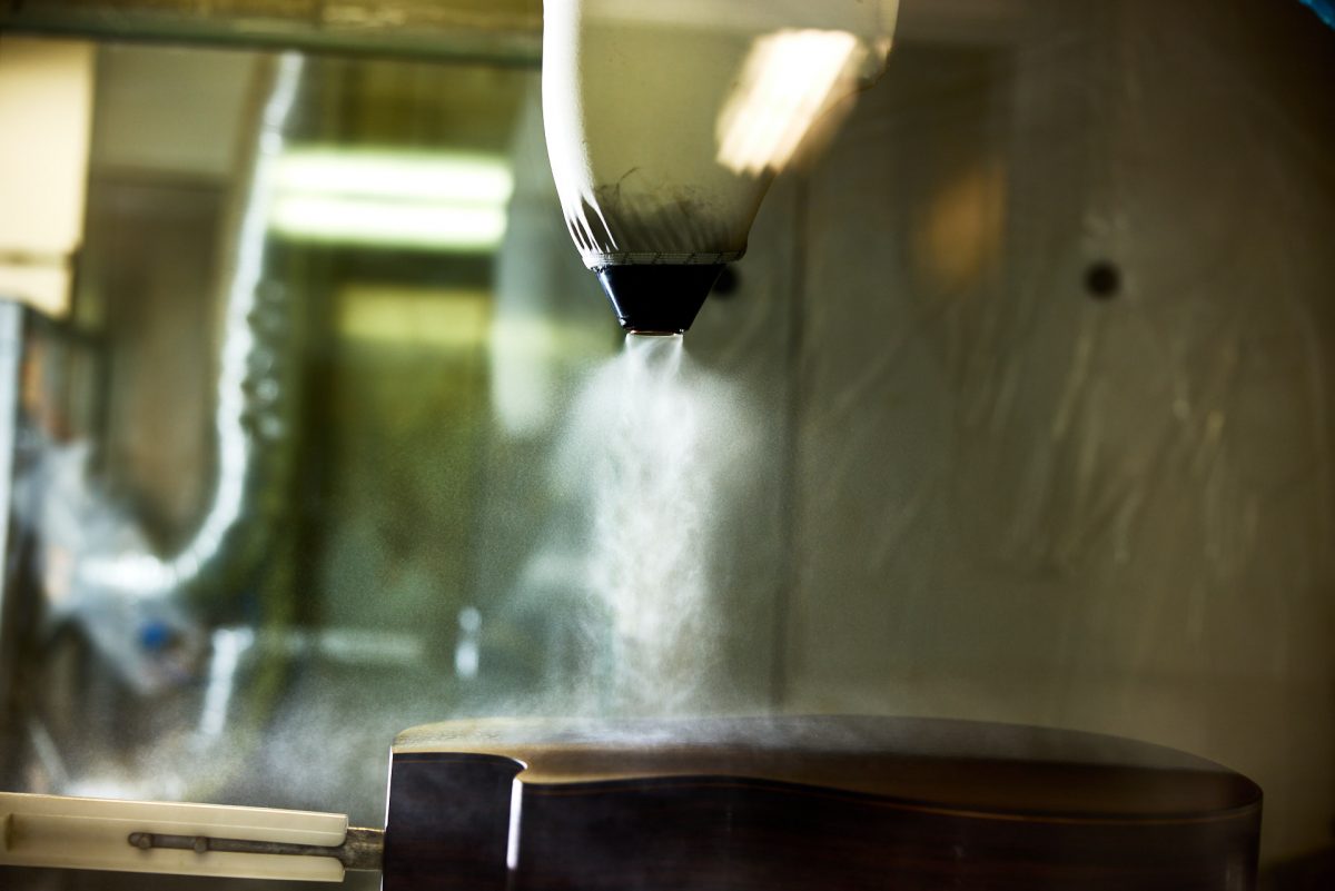 finish spraying machine applying finish mist to an acoustic guitar inside the Taylor factory