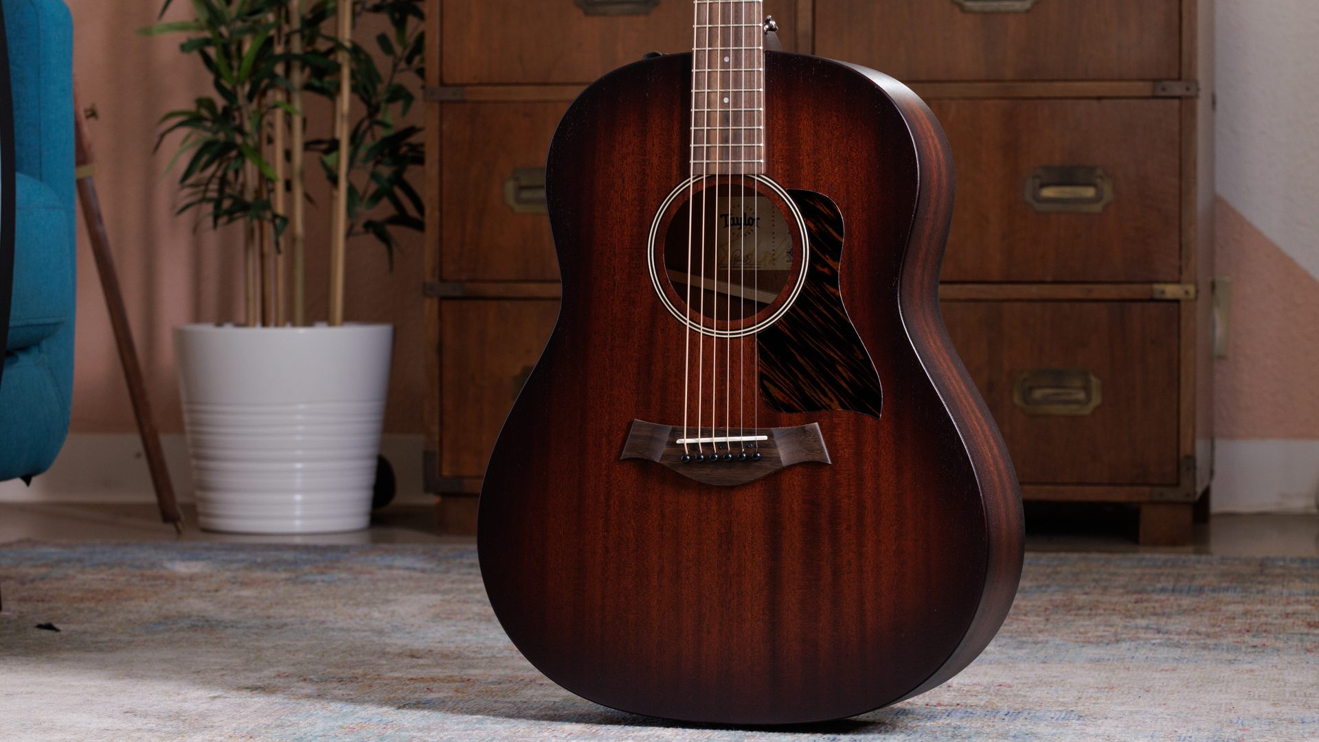 Image of American Dream Series AD27e acoustic-electric guitar with edgeburst finish standing upright in a living room environment